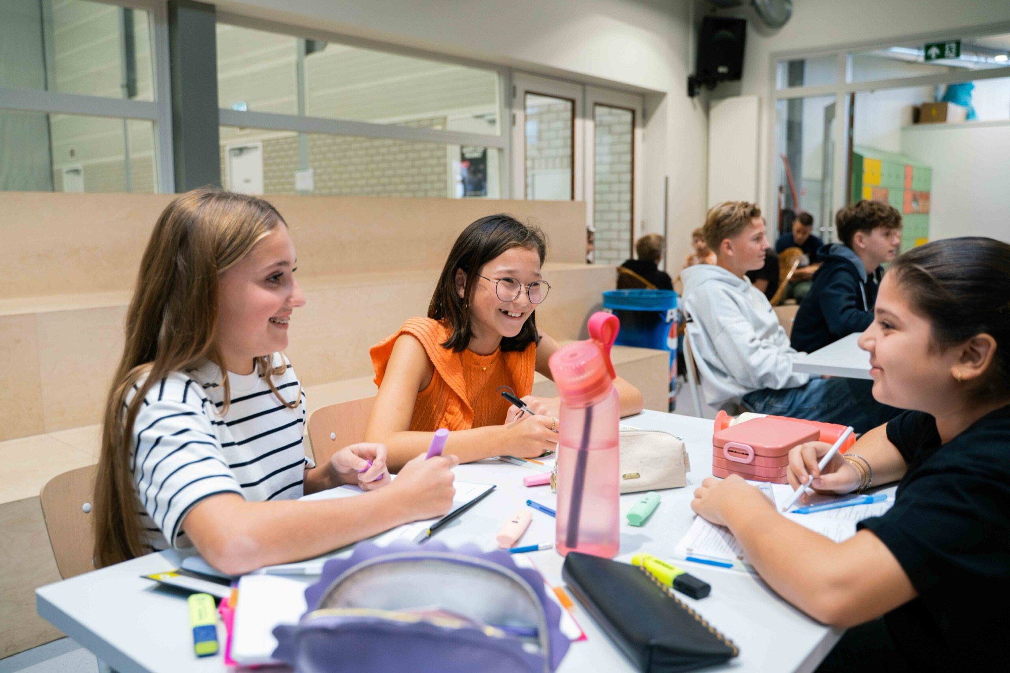 Leerlingen werken lachend samen aan een tafel in de aula van SG De Dijk.